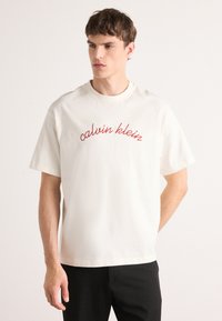 White cotton t-shirt with short sleeves and a crew neck. Features a red logo "calvin klein" embroidered on the front.