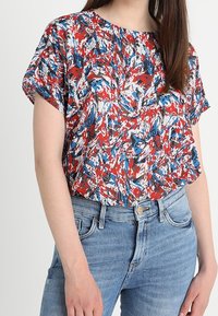 Rød, hvid og blå abstrakt mønstret kortærmet top med løs pasform og rund halsudskæring, paired med højtaljede blå denim jeans.