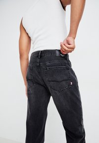 Zwarte denim jeans met een relaxed fit, voorzien van een label op de achterkant van de taille en twee achterzakken. De stof heeft een subtiele textuur.