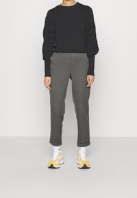 Svart tröja med puffiga, texturerade ärmar, tillsammans med olivgröna byxor. Vita och gula sneakers fulländar looken.