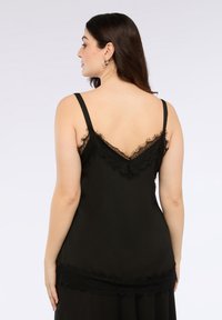 Camisola nera con spalline sottili, dotata di uno schienale a forma di V e delicati pizzi lungo i bordi e il collo, in un tessuto morbido e testurizzato.