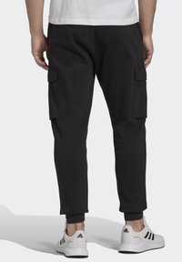 Svarte cargo joggere med en tapered fit, udstyret med sidelommer og ribbede manchetter, parret med hvide sportssko med sorte striber.