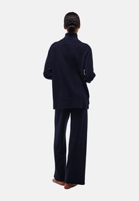 Pull en maille bleu marine avec un col haut, coupe décontractée ; associé à un pantalon large assorti, coutures minimales visibles, tissu texturé, pieds nus.