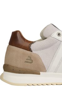 Zapatillas blancas y beige con una parte superior de malla texturizada, talón de cuero marrón y suela de goma clara. Costuras notables y logo en el costado.
