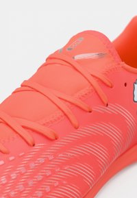 Lyseorange atletiksko med tekstureret overflade, tynde snørebånd og sølvfarvede detaljer. Ergonomisk form designet til ydeevne.