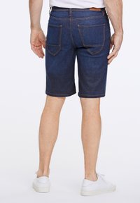 Shorts en denim bleu foncé, avec des poches arrière à coutures contrastées et une coupe droite, associés à des baskets blanches.