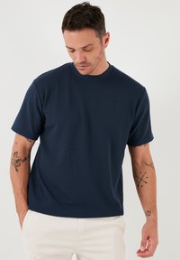 Sötétkék bordás, rövid ujjú póló kerek nyakkivágással. Texturált anyagból készült, laza fazonú, finom varrási részletekkel.