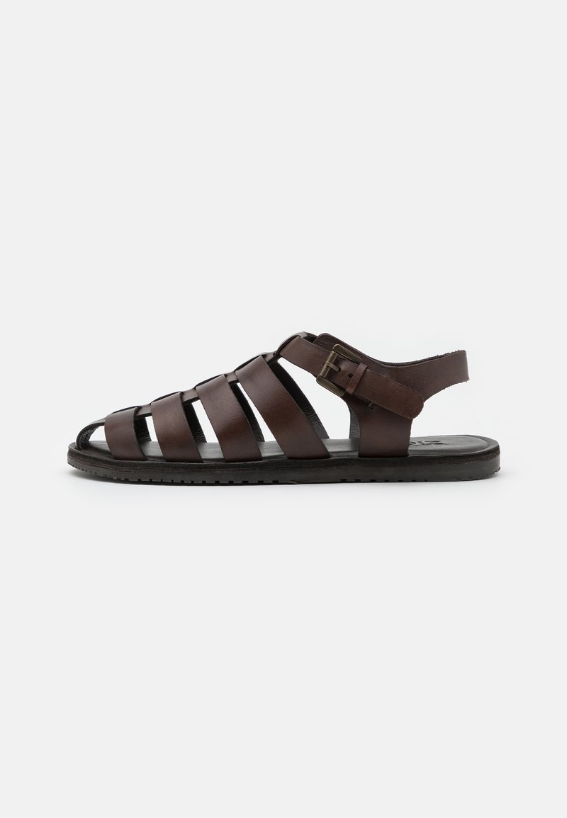Sandal de couro castanho com várias tiras largas, design de bico aberto, fecho de fivela no tornozelo e sola texturizada para aderência.