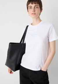 White cotton t-shirt with light blue "Calvin Klein" logo, paired with a black leather tote bag featuring a structured design and dual handles.
