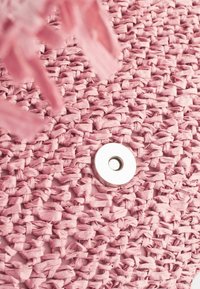 Gros plan sur un tissu rose tissé avec un bouton-pression magnétique blanc circulaire et des glands à franges roses.