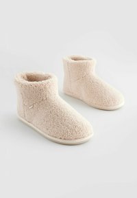 Pantoufles en polaire rose avec une texture douce, un design de hauteur intermédiaire et des semelles en caoutchouc beige, présentant une petite étiquette sur le côté.