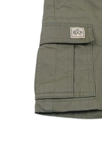 Khaki stof, cargo-stijl zak met klep, gestikte details en een merkpatch met gekruiste symbolen op het oppervlak.