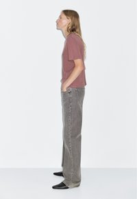 Rust-colored cotton t-shirt with short sleeves, paired with high-waisted, faded gray wide-leg jeans and black pointed-toe boots.