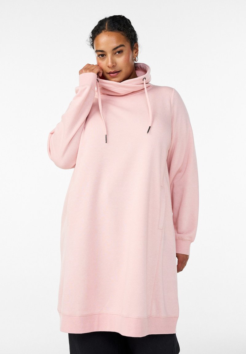 Abito felpa rosa chiaro con collo alto, coulisse, maniche lunghe e tasche laterali. Tessuto morbido, vestibilità comoda e lunghezza fino a metà coscia.