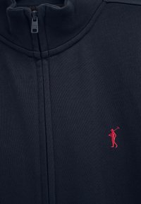 Pull zippé bleu marine avec un col montant et un petit logo brodé en rouge représentant un joueur de polo sur la poitrine.