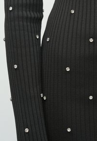 Fekete bordázott anyag, melynek felszínét apró, kerek, áttetsző strasszok díszítik.