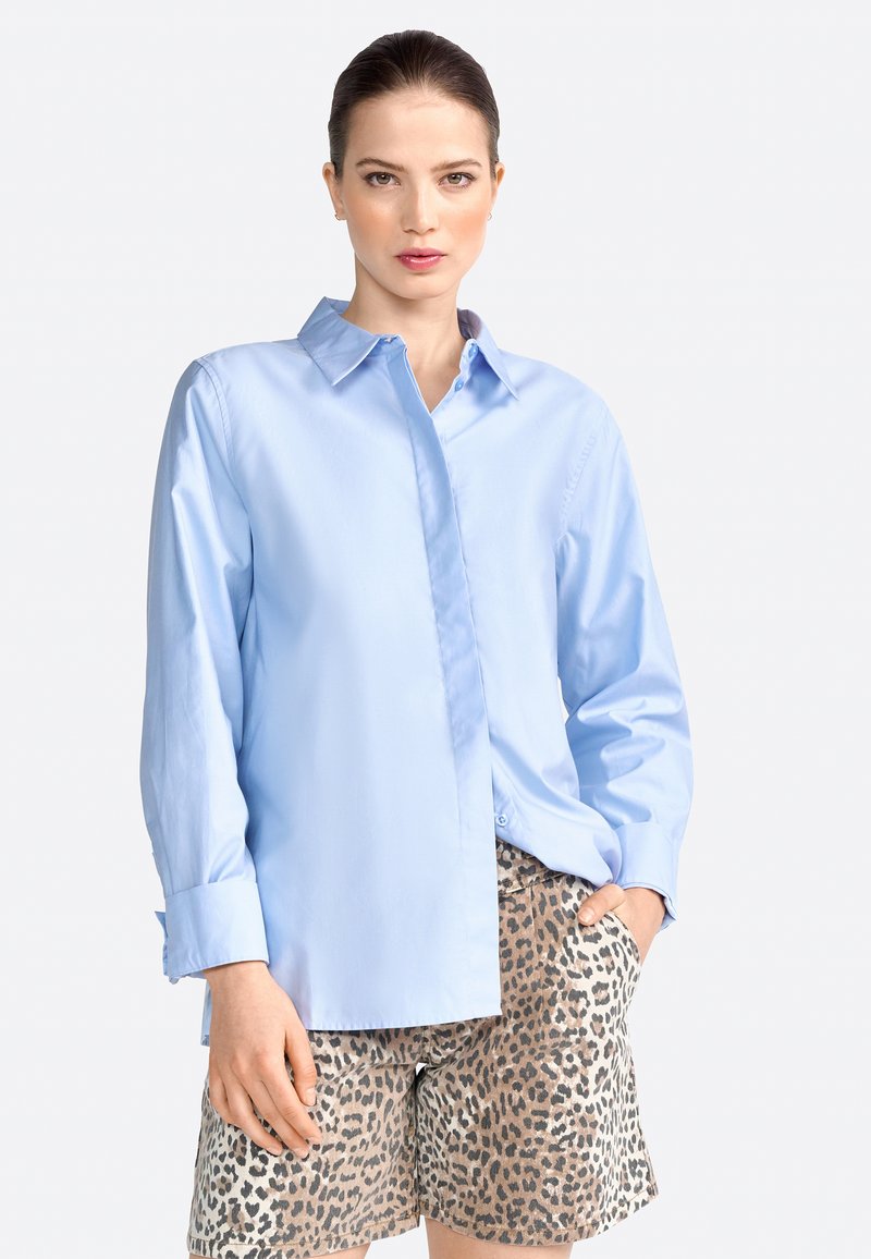 Lyseblå langærmet skjorte med knap-åben krave, parret med tan shorts med sort leopardprint. Glat stofstruktur.