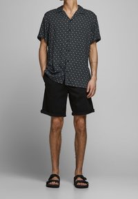 Kortärmad svart skjorta med diamantsmönster, kombinerad med svarta shorts med uppvikta ben och svarta sandaler. Lättviktig, avslappnad outfit.