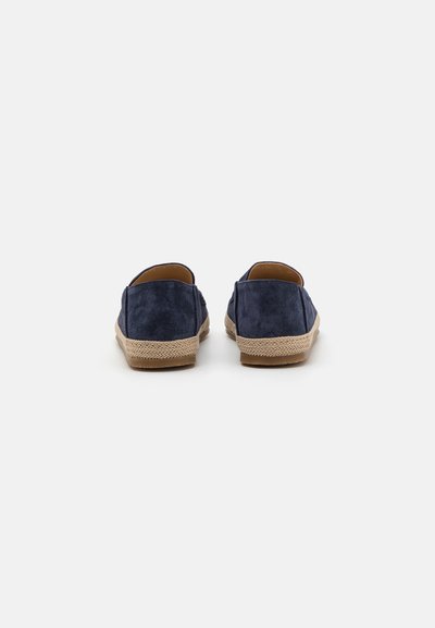 Chaussures en daim bleu marine avec un dos arrondi et des semelles en jute tissées. Le design présente un style à enfiler, une texture douce et des accents de tons neutres.