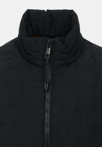 Fekete puffdzseki magas gallérral, elöl cipzárral és steppelt textúrával. Anyaga simának és könnyűnek tűnik. Minimalista design.