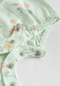 Light green floral onesie made from soft fabric, featuring small pink and yellow flowers, elastic edges, and metal snap closures.