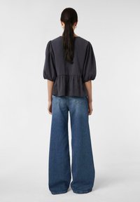 Dunkelgraues Oberteil mit Puffärmeln und Peplum-Taille, kombiniert mit weit geschnittenen blauen Jeans aus Denim, die dezente rückseitige Nähte zeigen.
