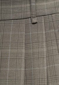 Šedá kostičkovaná látka s texturovanou vazbou, ve které se střídají tmavé a světlé linie a vytvářejí strukturovaný vzor. Viditelné zakládané sklady.