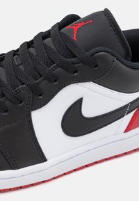 Baskets noir et blanc avec des accents rouges. Fabriquées en cuir lisse, elles présentent un logo Nike bien visible, des lacets texturés et une semelle en caoutchouc.