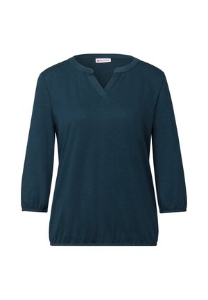 Tyrkysová halenka s dlouhým rukávem, výstřihem do V a elastickými manžetami. Vyrobena z měkké látky, s volným střihem a m írně rozšířeným lemem.