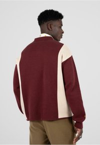 Maglione a blocchi di colore bordeaux e crema con vestibilità rilassata, polsini a coste e colletto ripiegabile. Texture morbida, spessore medio.