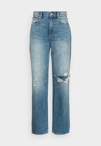 Jeans de denim azul desbotado com um corte largado, apresentando detalhes desgastados e remendos desfiados nos joelhos, além de um fecho clássico de botão.