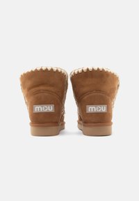 Stivali alla caviglia in pelle scamosciata marrone con un accento cucito color crema lungo la parte superiore, caratterizzati da una fodera beige testurizzata e una suola in gomma. Loghi visibili sul retro.