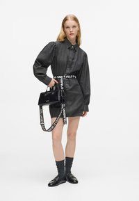 Czarna, szara sukienka dżinsowa z paskiem w talii, długimi bufkami i elegancką, czarną torebką na ramię z logowanym paskiem. Czarne buty z akcentami.