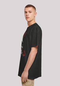 Camiseta negra de manga corta, con un gráfico de una calavera y rosas, hecha de algodón con un corte relajado. Textura sutil.