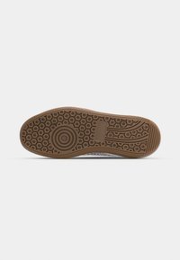 Suela de zapato de goma con patrones de dibujo circulares y lineales. Color marrón con una superficie texturizada. Presenta un logo grabado en el lateral.