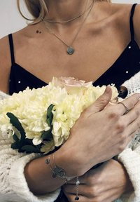 Top negro de tirantes con lunares blancos, collares de plata en capas, ramo de flores blancas y rosas, pulsera de plata con charms, suéter texturizado.