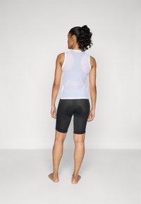 Weißes Netz-Tanktop kombiniert mit schwarzen Radhosen, die über eine gepolsterte Sitzfläche, eine enge Passform und eine glatte Textur verfügen. Ansicht von hinten.