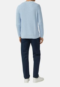 Helle blaue Strickjacke mit einem strukturierten Muster, Rundhalsausschnitt und gerippten Bündchen. Kombiniert mit dunkelblauen Hosen und weißen Sneakers.