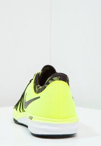 Neon žlutá a černá sportovní obuv s logem Nike, prodyšný svršek a polstrovaná bílá podešev, pohled zezadu na bílé ploše.