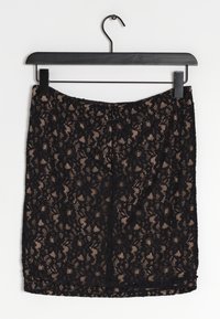 Jupe crayon en dentelle noire avec un motif floral, texture transparente, et une longueur finissant au-dessus du genou ; suspendue à un cintre noir.