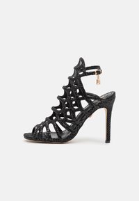 Svarta högklackade sandaler med öppen remdesign, texturerat material och ankelrem, med en liten metallisk accent.