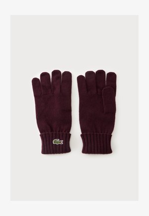 Paire de gants tricotés violet foncé avec poignets côtelés et logo crocodile vert sur le poignet du gant gauche, posés à plat sur fond blanc.