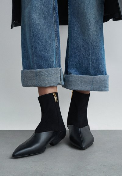 Czarne botki na kostkę wykonane z gładkiej skóry i teksturowanego zamszu. Złoty detal zamka błyskawicznego i szpiczasty nosek.