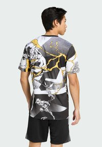 Koszulka z krótkim rękawem z nadrukiem w stylu komiksowym w kolorach czarnym, białym i żółtym, przedstawiająca postacie i dynamiczne wzory.