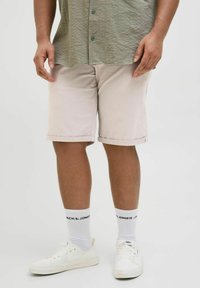 Jasnobeżowe szorty z podwiniętymi nogawkami, w połączeniu z białymi tenisówkami i skarpetkami z napisem "JACK & JONES" w czarnym kolorze.
