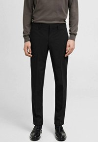 Schwarze, taillierte Hosen aus gewebtem Stoff, mit flachem Bund, seitlichen Taschen und einer glatten Textur, ergänzt durch glänzende schwarze Loafers.
