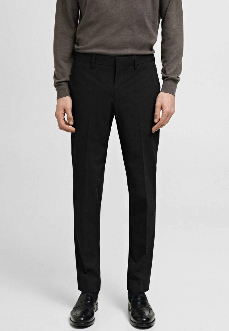 Schwarze, taillierte Hosen aus gewebtem Stoff, mit flachem Bund, seitlichen Taschen und einer glatten Textur, ergänzt durch glänzende schwarze Loafers.