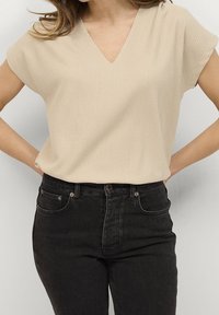 Beige v-neck short-sleeve top with textured fabric, paired with high-waisted black jeans featuring classic pocket design.