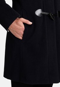 Námořnický vlnený kabát so zapínaním na gombík, ktorý má vrecko po boku a hladký povrch. Rysy zahŕňajú kožený uzáver a podšívku.