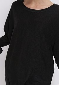 Schwarzer, locker sitzender Pullover aus weichem Material, mit weitem Ausschnitt und überschnittenen Schultern, der eine glatte Textur und minimale Details aufweist.